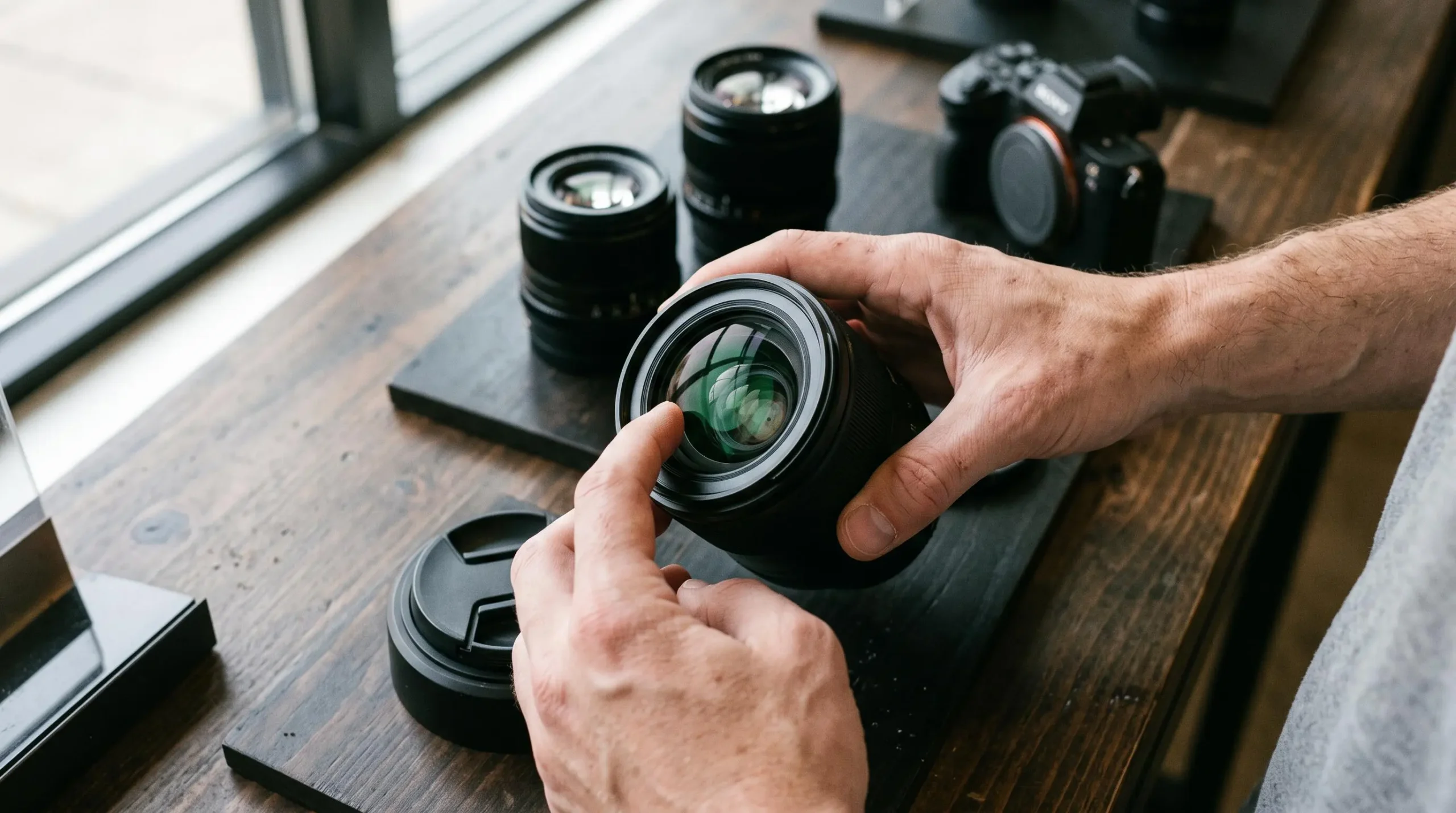 Gros plan sur des mains examinant un objectif photo lumineux posé sur une table de présentation.